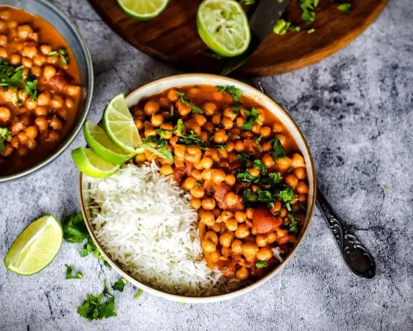 Herzhafte Kichererbsen Rezepte: Ein Teller mit Reis und Kichererbsen-Curry, garniert mit Limettenspalten und Koriander.