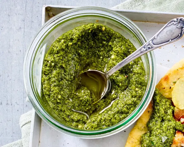 Frisches Basilikum Pesto in einem Glas, mit einem Löffel darin. Perfekt für Pasta oder Bruschetta.