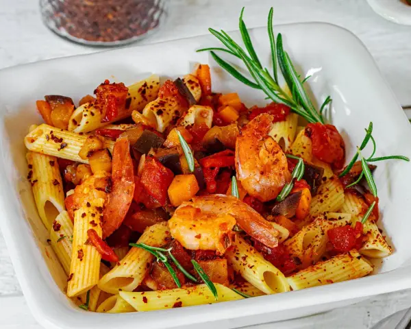 Penne-Nudeln mit Garnelen, Auberginen und Tomaten, garniert mit Rosmarin und Chiliflocken. Ein köstliches Gericht, das Lust auf mehr macht.