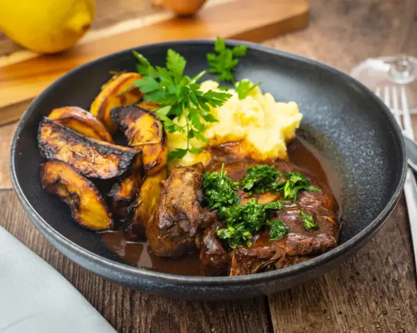 Herzhaftes Osso Buco, eine **beinscheibe italienisch** zubereitet, serviert mit cremigem Kartoffelpüree und gerösteten Kartoffelspalten.