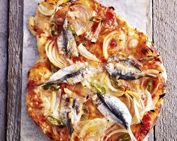 Eine rustikale Sardellen Pizza mit Zwiebeln und grünen Paprikastreifen, auf einem Holzbrett serviert.