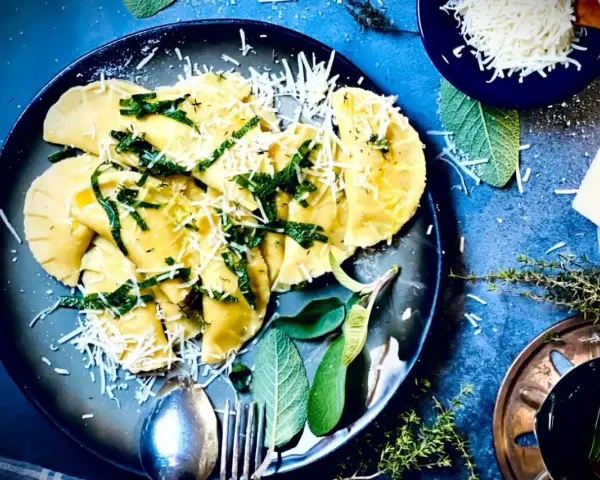 Frische Ravioli, ein italienisches Gericht, mit geriebenem Parmesan und Kräutern garniert. Das Ravioli-Teig Rezept italienisch ist hier perfekt umgesetzt.