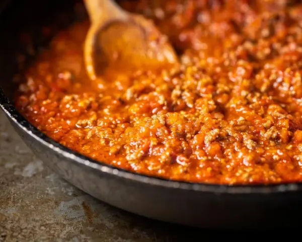 Herzhafte Bolognese-Sauce köchelt in einer Pfanne, die Zutaten für ein perfektes Pastagericht. Ein Holzlöffel rührt die köstliche Masse.