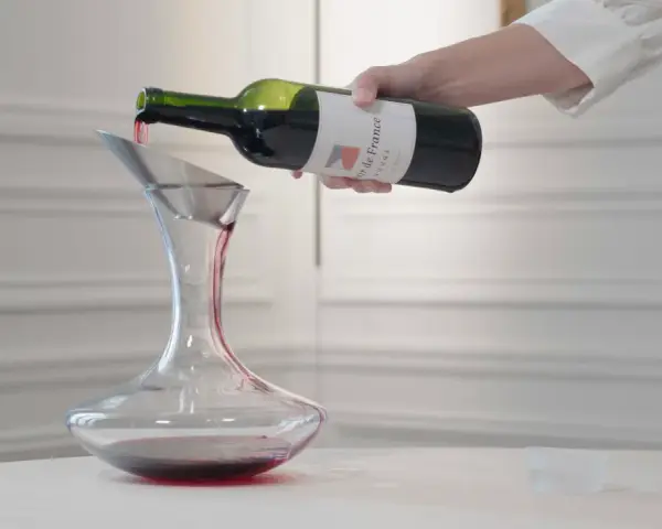 Roter Wein wird aus einer Flasche in einen Dekanter gegossen. Der Wein ist verkorkt und bereit zum Genießen.