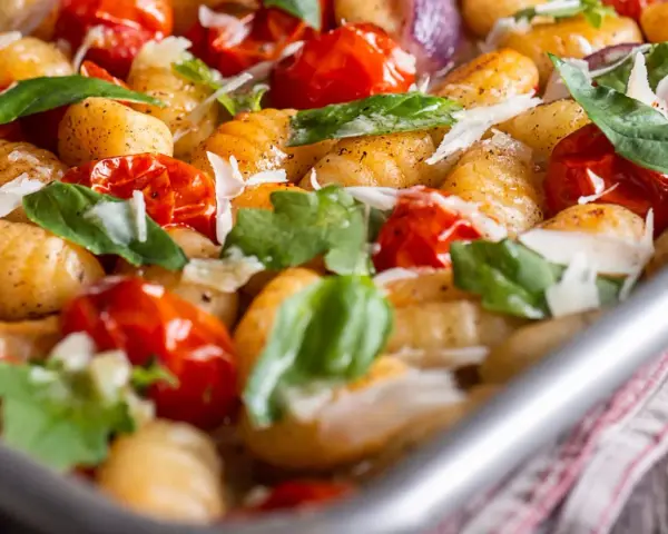 Gebackene Gnocchi mit Kirschtomaten, Basilikum und Parmesan. So sehen köstliche Gnocchi aus, wenn sie im Ofen mit frischen Zutaten zubereitet werden.