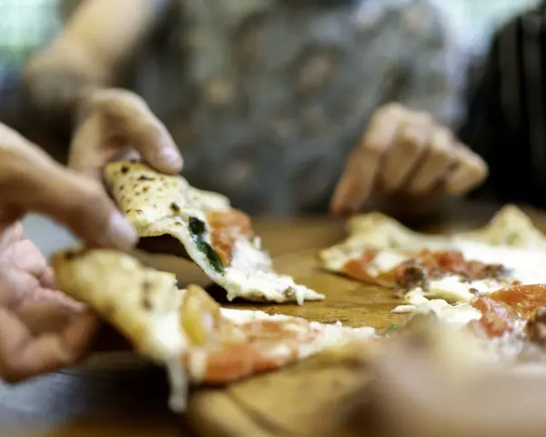 Hände greifen nach dampfenden Pizzastücken. So wie essen Italiener Pizza: gemeinsam, genussvoll, mit Freunden.