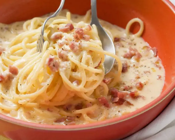 Cremige Pasta mit Ei und Speckwürfeln, ein klassisches italienisches Gericht, serviert in einer orangen Schüssel.