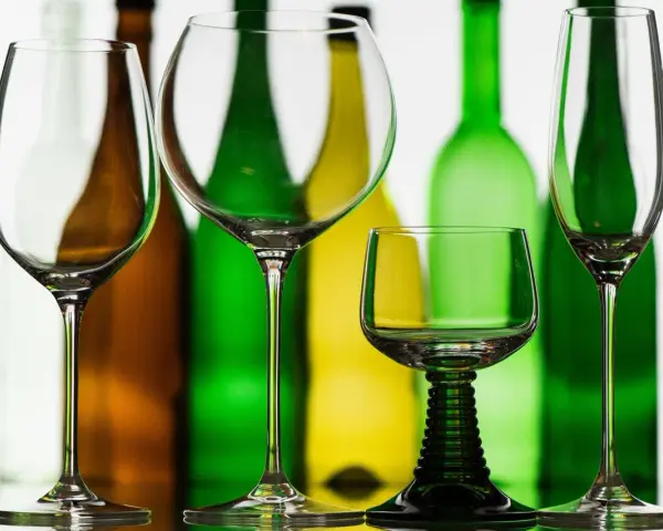 Leere Weingläser stehen vor bunten Flaschen. Perfekt, wenn man Wein kalt trinkt.