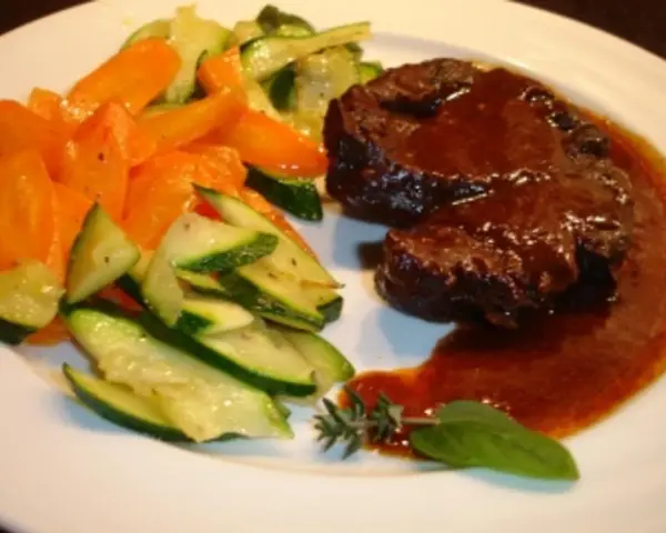 Ossobuco vom Rind auf sizilianische Art, zart geschmort in dunkler Sauce, serviert mit Karotten und Zucchini.