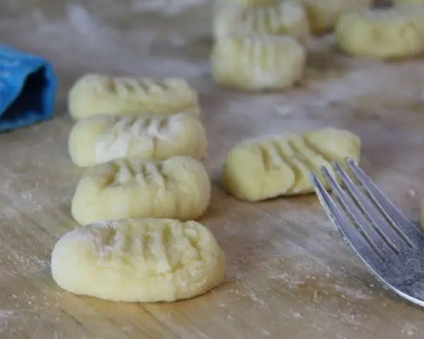 Frisch geformte italienische Gnocchi liegen auf bemehltem Holz. Eine Gabel und ein blauer Lappen sind ebenfalls zu sehen.