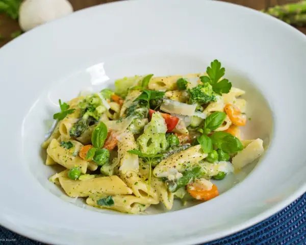 Penne mit cremigem Pesto, Spargel, Erbsen, Brokkoli und Karotten, garniert mit Parmesan und frischen Kräutern.