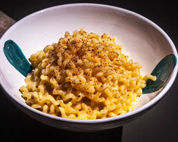 Cremige Pasta Alfredo, bestreut mit Gewürzen, in einer weißen Schüssel mit türkisfarbenen Akzenten.