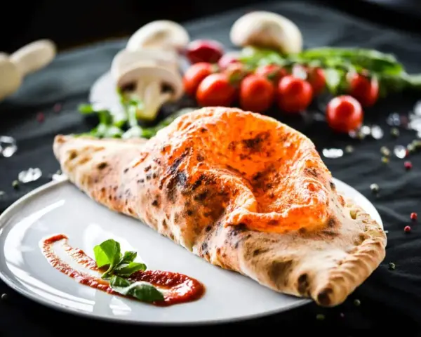 Ein goldbrauner, knuspriger Pizza Calzone mit geschmolzenem Käse und frischem Basilikum auf einem Teller.
