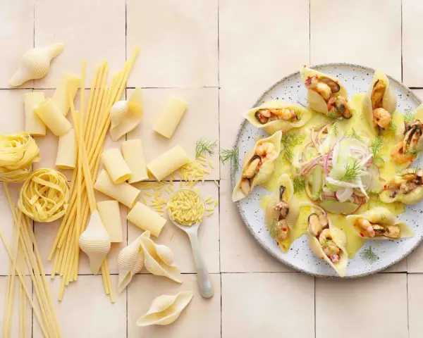 Gefüllte Conchiglioni mit Meeresfrüchten, ein köstliches italienisches Rezept. Daneben verschiedene italienische Pasta-Sorten.