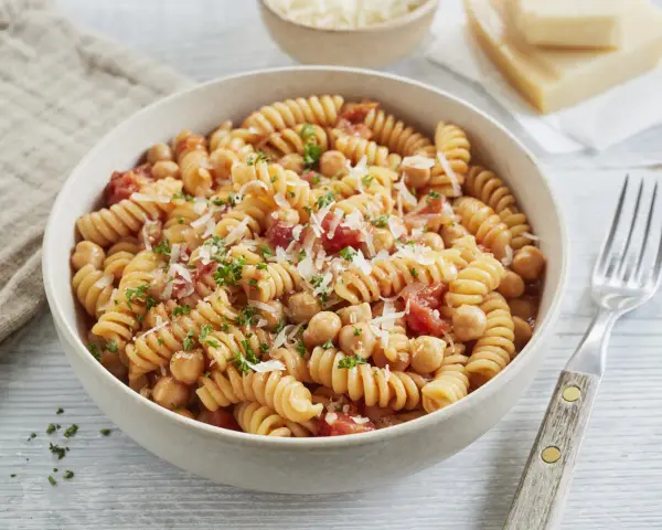 Eine Schüssel Fusilli-Nudeln mit Kichererbsen, Tomaten und Parmesan, garniert mit Petersilie.