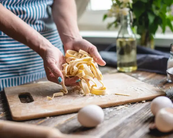 Frische Pasta aus dem perfekten pasta teig rezept. Hände halten die Bandnudeln, Mehl und Eier liegen bereit.
