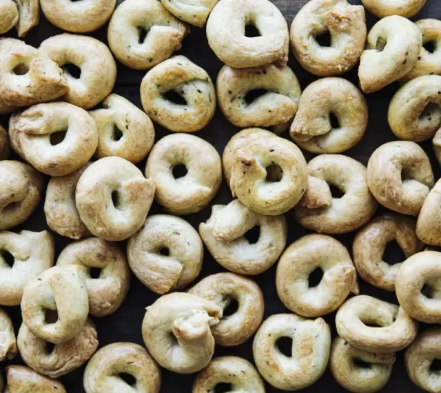Viele goldbraune Taralli, die nach einem einfachen Taralli Rezept gebacken wurden, liegen dicht beieinander auf dunklem Holz.