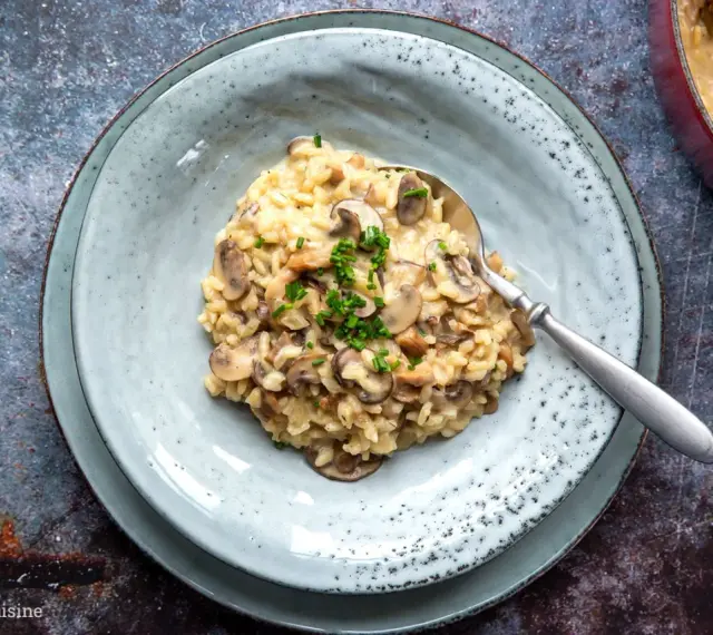 Cremiges Pilzrisotto, ein köstliches risotto rezept, garniert mit frischen Kräutern, auf einem Teller mit Löffel.