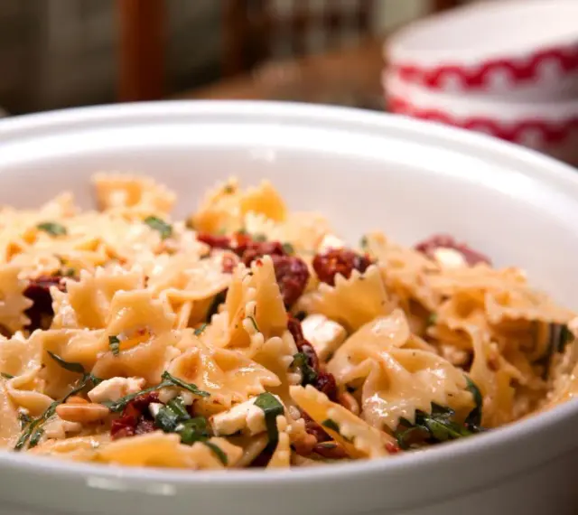 Ein köstlicher italienischer Nudelsalat mit Farfalle, getrockneten Tomaten, Feta und Kräutern in einer weißen Schüssel.