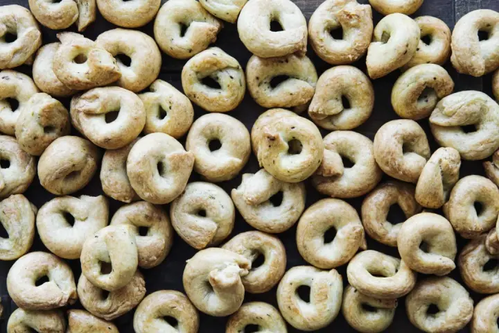 Viele goldbraune Taralli, die nach einem einfachen Taralli Rezept gebacken wurden, liegen dicht beieinander auf dunklem Holz.