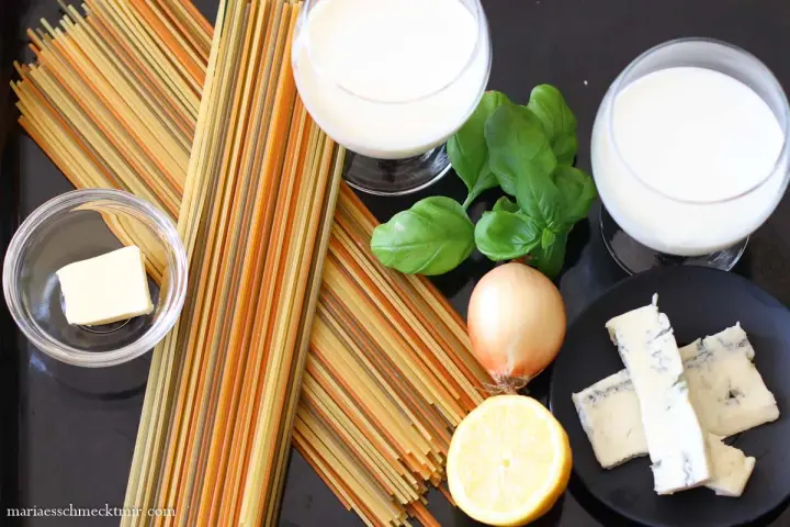 Zutaten für eine cremige Gorgonzola-Sauce: bunte Spaghetti, Butter, Zwiebel, Zitrone, Basilikum und Gorgonzola.