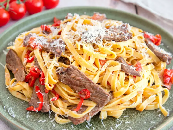 Pasta mit Rinderfiletstreifen, Tomaten und Parmesan auf einem grünen Teller.