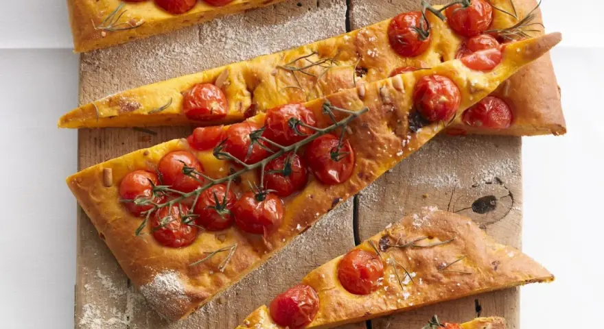 Saftige focaccia mit tomaten und Rosmarin, auf einem Holzbrett mit Mehl bestäubt.