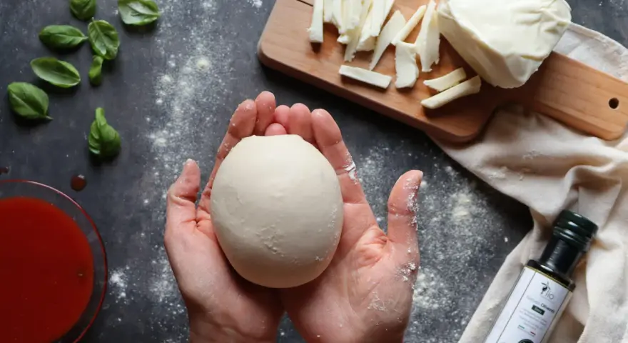 Hände formen Teig für ein Caputo Nuvola Rezept. Mozzarella, Basilikum und Tomatensauce liegen bereit.