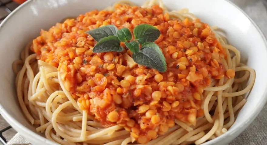 Herzhafte rote Linsen Bolognese auf Spaghetti, garniert mit frischen Kräutern. Ein köstliches und gesundes Gericht.