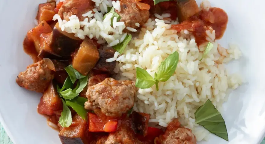 Herzhafte Salsiccia-Zubereitung in der Pfanne mit Auberginen, Paprika und Reis, garniert mit frischem Basilikum.
