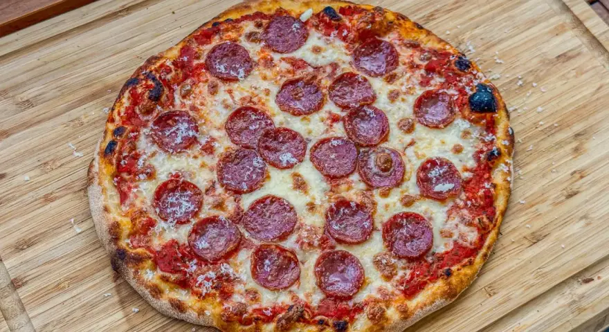 Eine köstliche Pizza Salami mit geschmolzenem Käse und knusprigem Rand liegt auf einem Holzbrett.