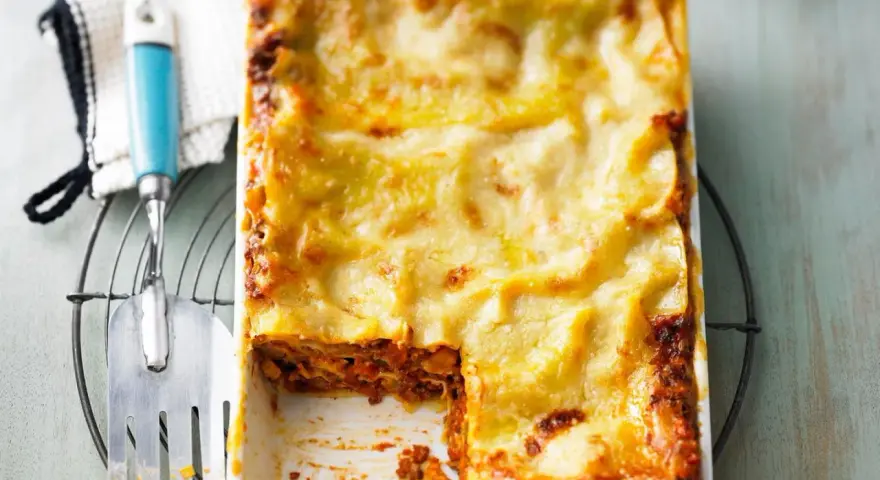 Eine frisch gebackene, italienische Lasagne in einer Auflaufform, mit einer goldbraunen Käseschicht und einem Stück herausgenommen.