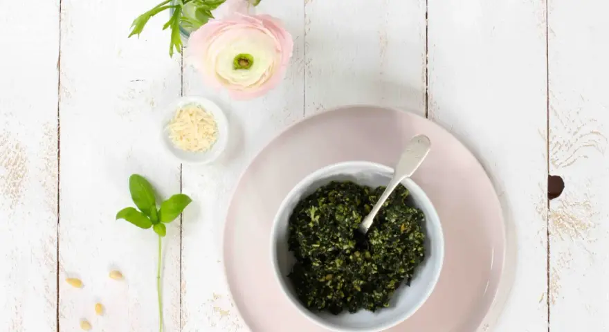 Schüssel mit frischem Basilikum-Pesto, Pinienkernen, Parmesan und einer zarten rosa Blume. Ein Hauch des originalrezepts.