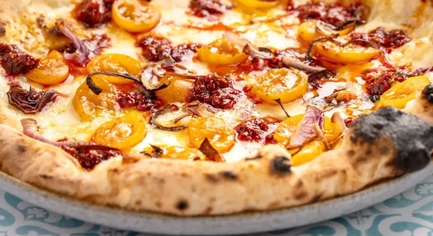 Eine köstliche Nduja Pizza mit geschmolzenem Käse, gelben Tomaten und roten Zwiebeln.