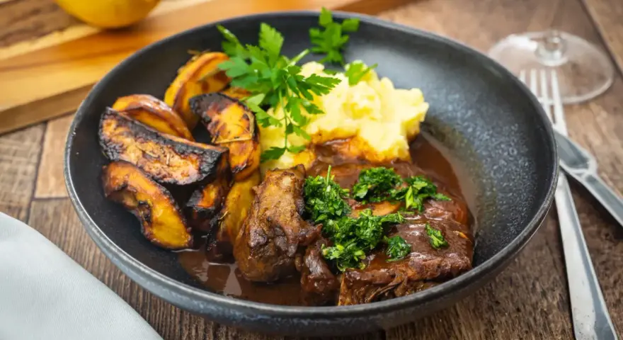 Ein Teller mit dem originalen Ossobuco-Rezept, dazu Kartoffelpüree und geröstete Kartoffelspalten.