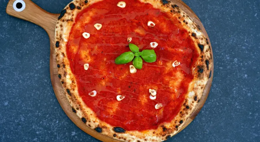 Eine klassische Pizza Marinara mit Tomatensauce, Knoblauch und frischem Basilikum auf einem Holzbrett.