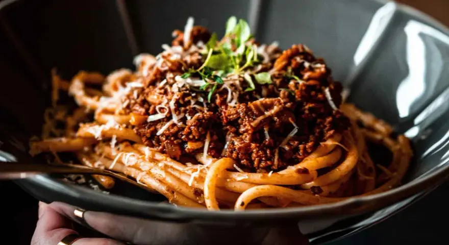 Eine Schüssel mit Pasta und original italienischer Tomatensauce mit Fleisch, garniert mit Parmesan und frischen Kräutern.