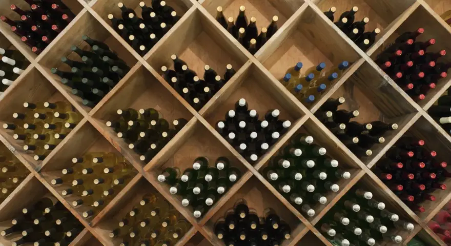 Weinregal mit vielen Flaschen Wein. Die Frage, wie lange kann man Wein lagern, hängt von der Sorte ab.