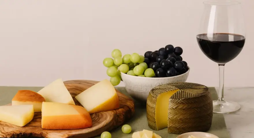 Käseplatte mit verschiedenen Käsesorten, Trauben und einem Glas Rotwein. Was bedeutet Primitivo bei Wein? Oft ein vollmundiger, fruchtiger Rotwein, der gut zu Käse passt.