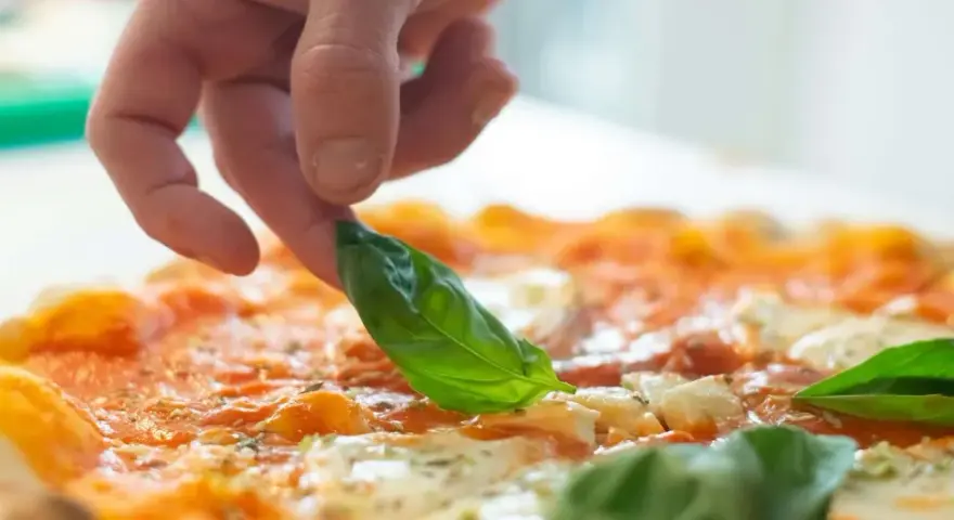 Eine Hand belegt eine Pizza mit frischem Basilikum. Die Pizza belegen reihenfolge ist wichtig für den perfekten Geschmack.