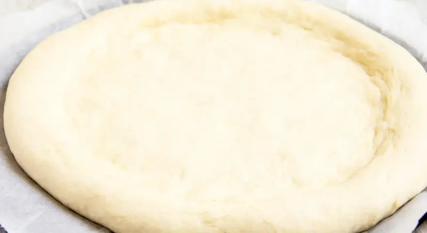 Ein runder, flacher Pizzaboden aus einem Pizzateig Rezept mit frischer Hefe, bereit für Belag und Backen.
