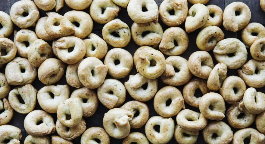 Viele goldbraune Taralli, die nach einem einfachen Taralli Rezept gebacken wurden, liegen dicht beieinander auf dunklem Holz.