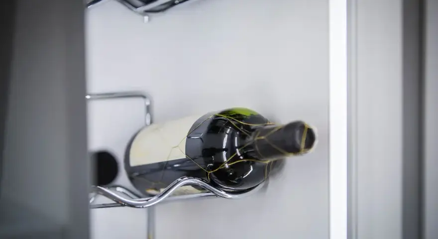 Eine Flasche Rotwein liegt auf einem Chromgestell. Der Wein ist bereits geöffnet, was man an der leichten Oxidation erkennen kann.