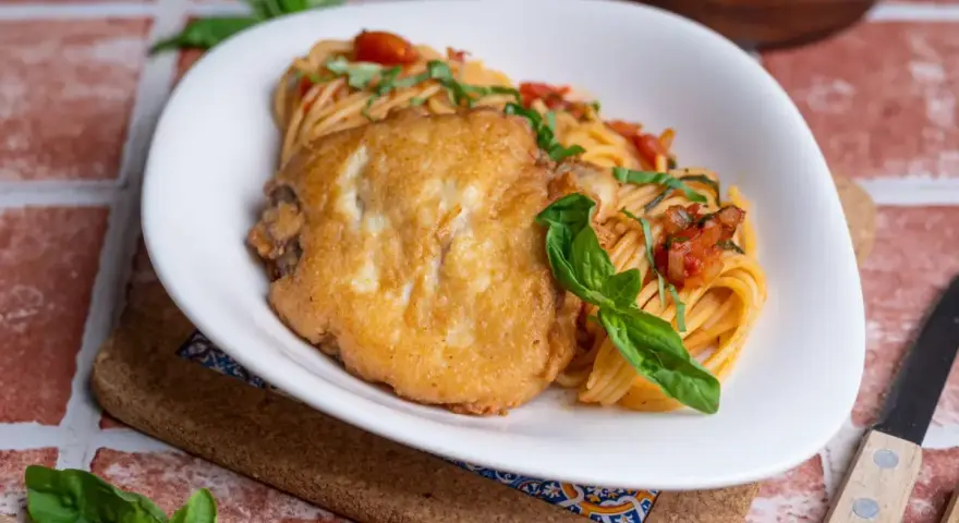 Ein paniertes Hähnchenfilet auf Spaghetti mit Tomatensoße und Basilikum. Ein Gericht, das an Piccata erinnert, aber ohne Zitrone.