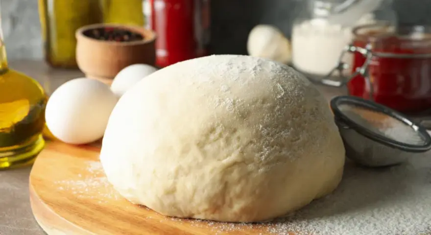 Frischer, fluffiger Teig für schnellen Pizzagenuss liegt bereit. Zutaten wie Eier, Öl und Gewürze deuten auf eine köstliche Pizza hin.