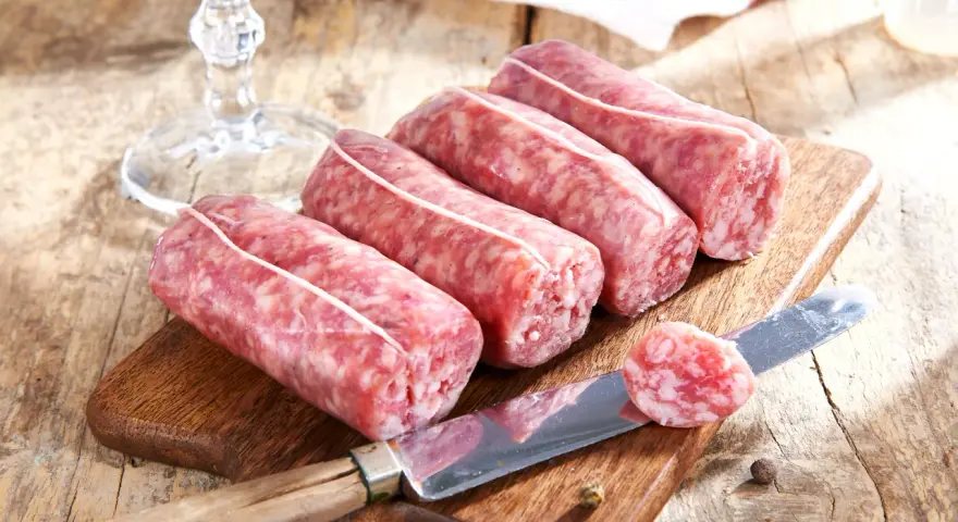 Frische Salsiccia zum Zubereiten liegen auf einem Holzbrett. Ein Messer mit einer Scheibe daneben deutet auf die Vorbereitung hin.