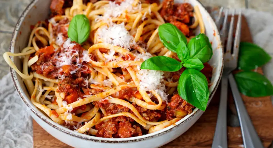 Eine Schüssel mit Linguine und einer herzhaften, **schnellen Bolognese**, garniert mit frischem Basilikum und Parmesan.