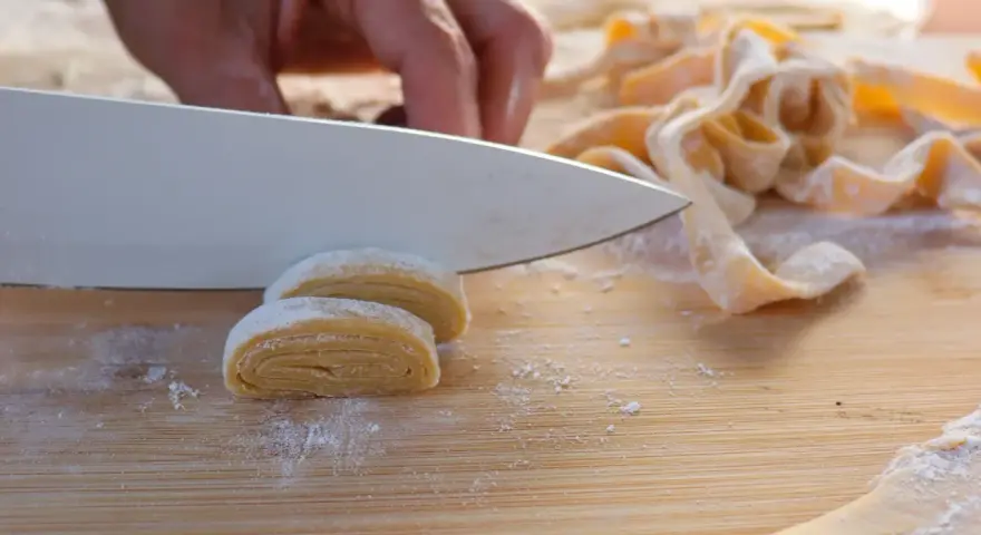 Hand schneidet frisch zubereitete, selbstgemachte Pasta auf einem Holzbrett.