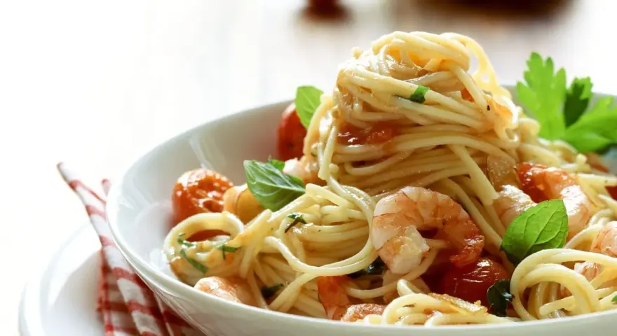 Ein Teller mit köstlichen Spaghetti mit Garnelen, Kirschtomaten und frischem Basilikum, appetitlich angerichtet.