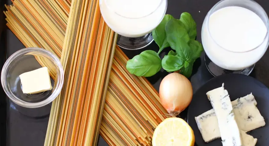Zutaten für eine cremige Gorgonzola-Sauce: bunte Spaghetti, Butter, Zwiebel, Zitrone, Basilikum und Gorgonzola.